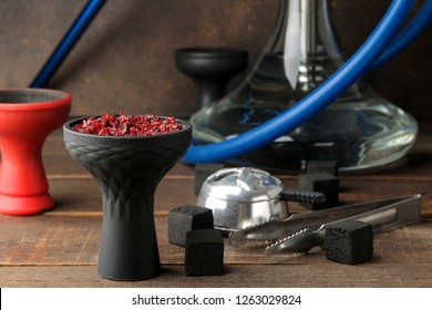 silicone bowl for hookah with tobacco and various accessories for making hookah. coals, tongs, kolaud on a brown wooden table. close-up. accessories for hookah.