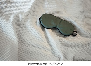 Silk Green Eye Mask Lying On The White Bedding In The Morning, Top View. Sleeping Concept.