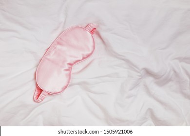 Silk Pink Eye Mask Lying On The White Bedding In The Morning, Top View. Sleep Well Concept.