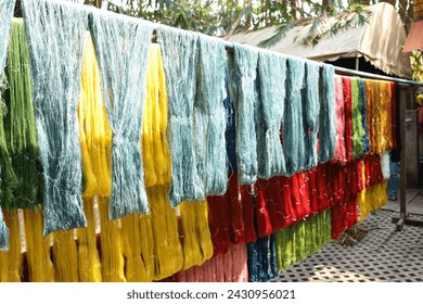 Silk threads hang in the sunlight. Rows of silk threads dyed with natural dyes hung on bamboo rods to dry in the sunshine in Thailand with copy space with selective focus.
