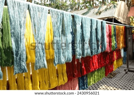Silk threads hang in the sunlight. Rows of silk threads dyed with natural dyes hung on bamboo rods to dry in the sunshine in Thailand with copy space with selective focus.