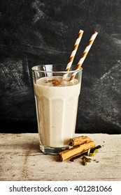 Silky Dairy Drink In Tall Glass With Two Swirl Colored Straws On A Long Rustic Table With A Sprinkle Of Cinnamon