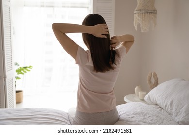 Silky waterfall. Rear view of calm content millennial female doing daily haircare procedure at morning in bedroom brushing combing soft long thick hair locks preparing to make beautiful stylish hairdo