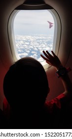 A Sillhouette Of A Boy Waving The White Cloudy Skies Through The Window Of A Flying Airplane