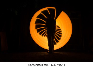 Sillhouette People Standing Alone With Yellow Circle Light Painting As The Backdrop