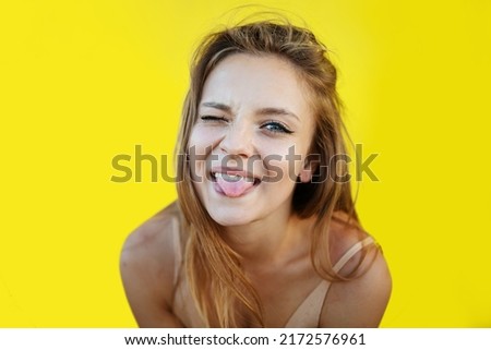 Silly blonde woman making funny face. positive girl acts on the camera, blinks, sticks out her tongue.