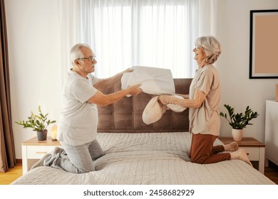 Silly childish old couple having pillow fight on a bed at comfortable apartment. Senior couple having fun - Powered by Shutterstock