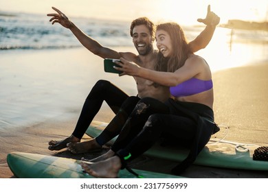 A silly couple on surfboards taking selfies on a shore. - Powered by Shutterstock