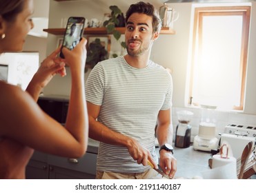 Silly, goofy and interracial couple taking pictures, having fun and cooking together in the kitchen at home. Happy girlfriend taking pictures of boyfriend, making funny faces and preparing dinner
