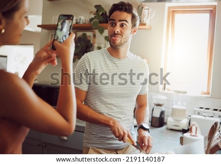 Silly, goofy and interracial couple taking pictures, having fun and cooking together in the kitchen at home. Happy girlfriend taking pictures of boyfriend, making funny faces and preparing dinner