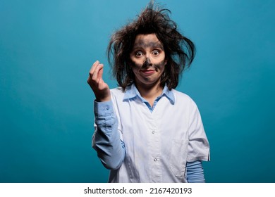 Silly Looking Crazy Chemist With Dirty Face And Messy Hair Looking At Camera On Blue Background. Mad Scientist With Hilarious Funny Look After Laboratory Chemical Explosion. Studio Shot.