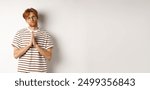 Silly redhead man asking for help, holding hands in pleading gesture and pucker lips, say please while begging you, standing over white background.