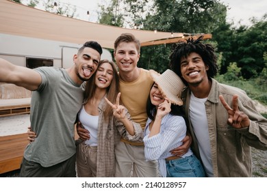 Silly young diverse friends posing near camper van in countryside, making different gestures, taking selfie on camping trip. Cheerful millennial people spending summer holidays in nature - Powered by Shutterstock