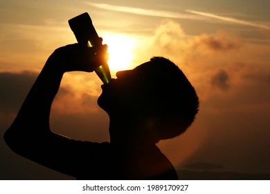 Silouhette of a man drinking beer from a bottle in the light of the sunset. Holiday lifestile image - Powered by Shutterstock