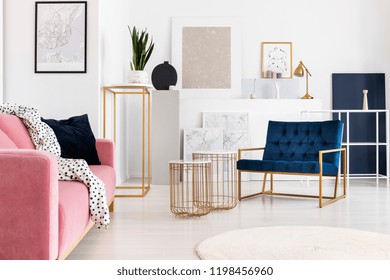 Silver Abstract Painting On The Wall Of Trendy Living Room With Two Elegant Coffee Tables, Petrol Blue Armchair And Powder Pink Couch With Doted Blanket On It