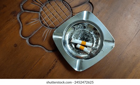 Silver ashtray, cigarette butts and ashes on a brown wooden table