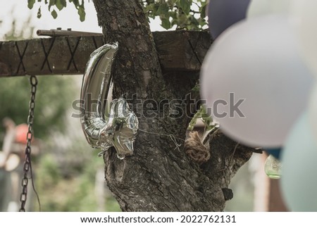 silver balloon number four tied to a tree with a rope and in the background still usually balloons in blue, gray and white as a children's party decor