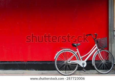 A silver bike parking in front of a red wall. 