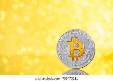 Silver bitcoin coin with golden bitcoin symbol on golden shiny glitter background