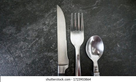 silver and black cutlery on gray quartz background, knife, fork and spoon