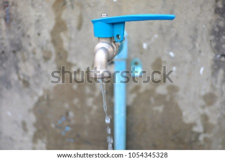 Silver blue steel faucet with flowing water and blur dirty cement wall of the building for saving water concept