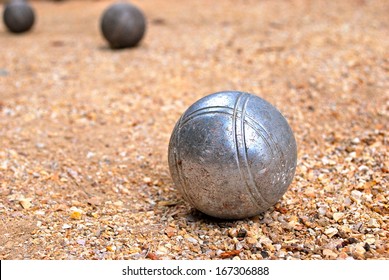 Silver Bocce Ball On Gravel Court With Two Darker Bocce Balls In The Background