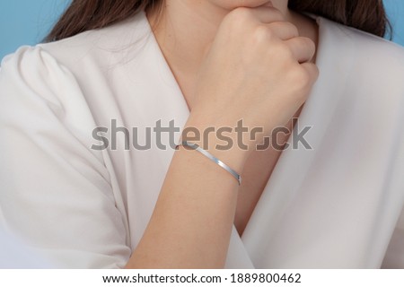 Silver bracelet with chain attached on women's wrist with white clothes and nail polish