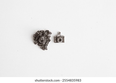 A silver camera charm designed with a nostalgic touch. Presented simply on a white background, this photograph symbolizes the longing for the past and the timeless magic of photography.