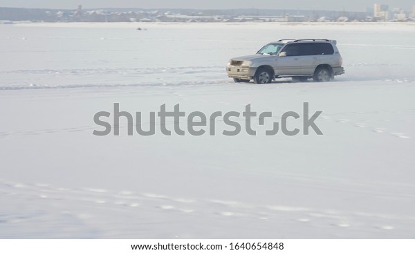 silver car drives by icy track\
on snow covered lake at winter.  Totota Land Cruiser - car racing\
on snow race track in winter. Driving a race car on a snowy\
road.