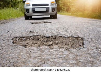 SIlver Car Driving On Highway And Approaching Big Deep Pothole. Concept Of Terrible Road, Road Needs Repairing