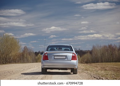 Silver Car On A Gravel Road Against A Blue Sky With Clouds. Back View. Car Journey.