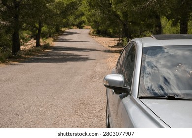 Silver car parked on an empty mountain asphalt road surrounded by green pine trees at Mirador del Garbi in Spain.