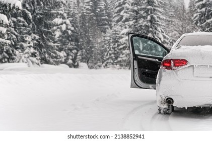 Silver Car Parked On Snow Covered Winter Road, Front Door Open, Blurred Trees Background, View From Behind