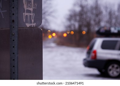 Silver car parked at in a rural park. Snow on the ground, Dusk, soft street lights in the distance. Up close street sigh ideal for editorial use