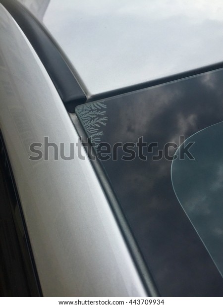 The silver car with tinted windows on the glass\
surface stripping windows.