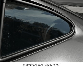 Silver car triangle window with chrome trim and tinted glass reflecting landscape view