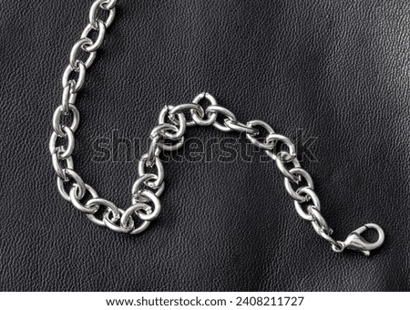 Silver chain on a black leather background.