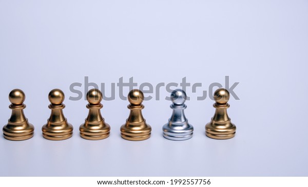 A silver chess piece that\
is different from the other gold chess pieces. concept of\
difference