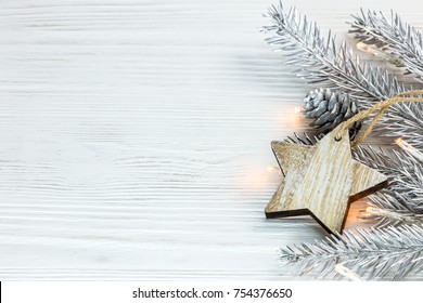 silver christmas tree branch with glowing garland and wooden star on white boards background - Powered by Shutterstock