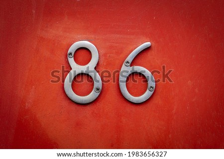 Silver chrome door number 86 eighty sic screwed onto wood painted bright red. Close up numerical sign. Foto stock © 