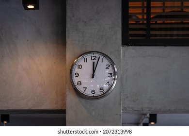 Silver chrome shiny white clock with a black arrow wall clock hangs on the concrete wall background.  Simple retro loft-style design and retro decoration background. Concept timing management.