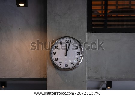 Silver chrome shiny white clock with a black arrow wall clock hangs on the concrete wall background.  Simple retro loft-style design and retro decoration background. Concept timing management.