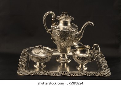Silver coffee set. Silver sugar bowl, coffee pot, a jug of milk. They stand on a silver platter. Black background.