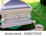 Silver coffin is placed on green cloth, ready for burial service during burial ceremony.