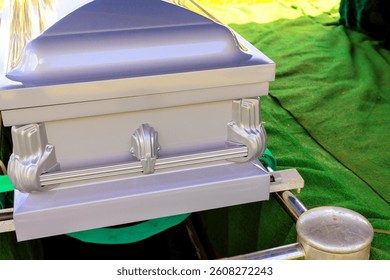 Silver coffin is placed on green cloth, ready for burial service during burial ceremony.