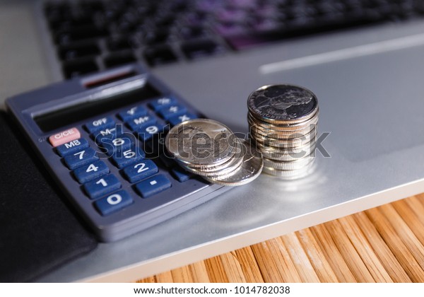 Silver coins stack with a calculator on grey\
notebook. Business, finance, saving money or car loan concept :\
coins stack, calculator and\
laptop