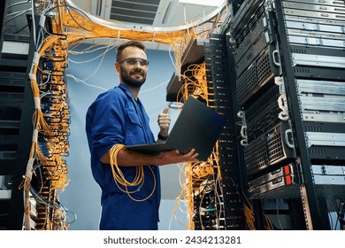 Silver colored laptop in hands. Young man is working with internet equipment and wires in server room. - Powered by Shutterstock