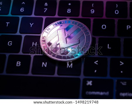 Silver cryptocurrency Litecoin laying on lit up qwerty keyboard of notebook or laptop with colorful reflection in coin. Virtual digital money with bokeh background and purple blue colors reflecting.
