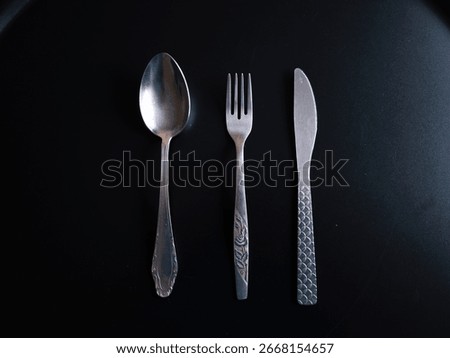 Silver cutlery, featuring a spoon, fork, and knife, arranged artfully on a dark surface, creates a minimalist and elegant table setting perfect for any dining occasion