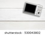 silver digital compact camera with blank black screen display place on white vintage wood table and top view with copy space